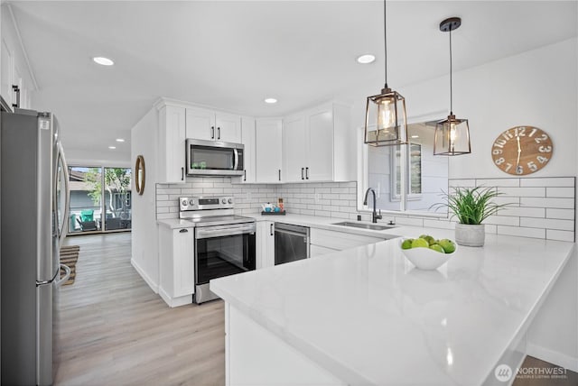 kitchen featuring a peninsula, a sink, white cabinetry, appliances with stainless steel finishes, and light wood-type flooring