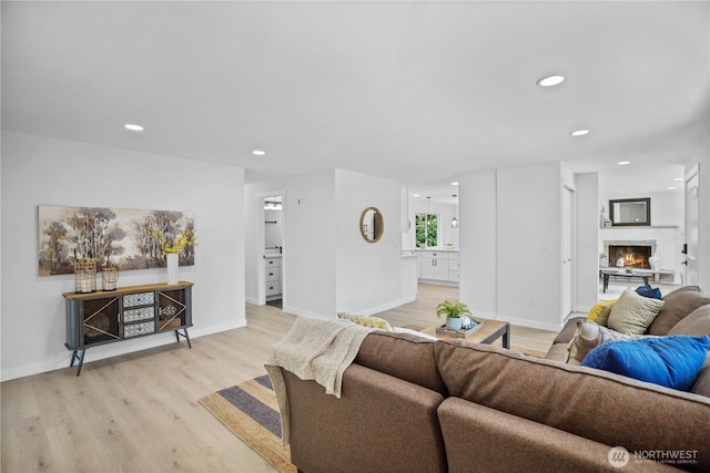 living room featuring light wood-type flooring, a fireplace, baseboards, and recessed lighting