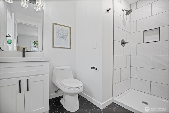 full bathroom with toilet, vanity, baseboards, tiled shower, and tile patterned floors