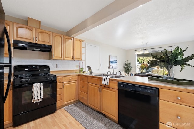 kitchen with light wood-style flooring, under cabinet range hood, light countertops, black appliances, and a sink