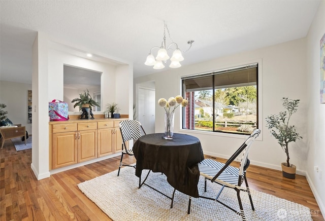 dining area featuring light wood finished floors, baseboards, and an inviting chandelier