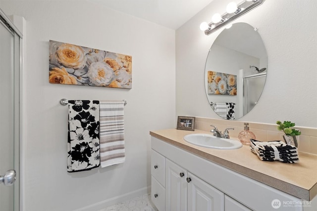 bathroom featuring a shower with shower door, baseboards, and vanity