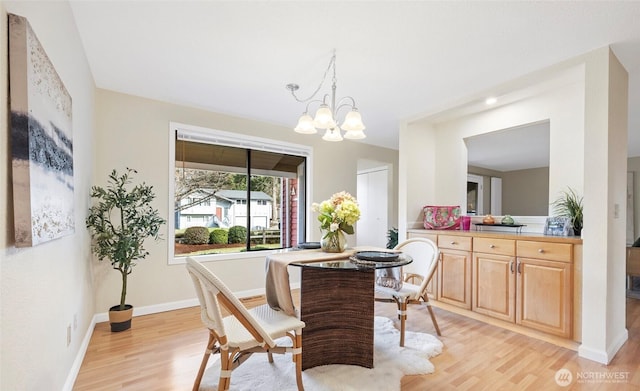 dining space with baseboards, light wood-type flooring, and an inviting chandelier