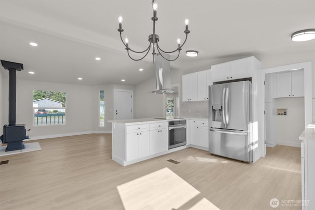 kitchen with stainless steel appliances, a peninsula, open floor plan, wall chimney exhaust hood, and a wood stove