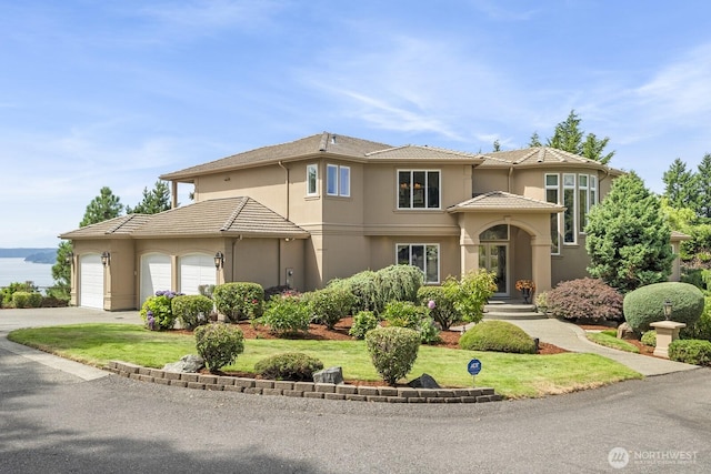 view of front of property featuring a garage, a tile roof, driveway, stucco siding, and a front lawn