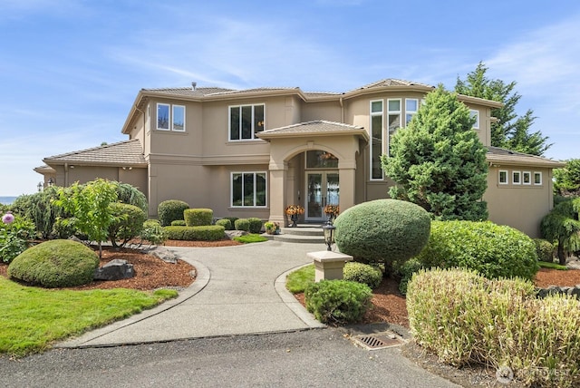 view of front facade with driveway, stucco siding, a tiled roof, and french doors