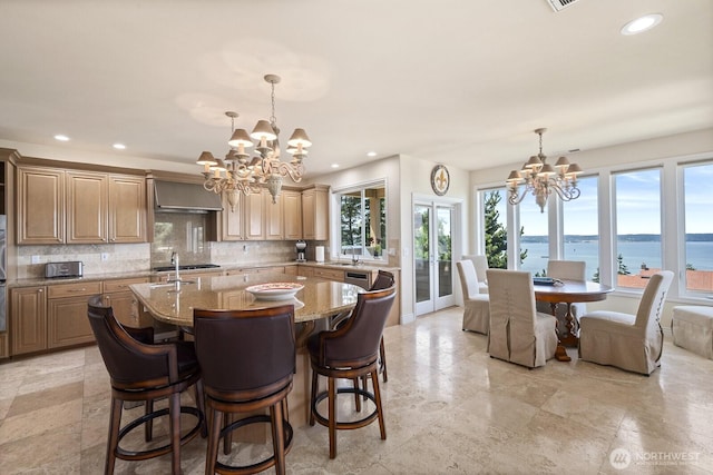 kitchen with a kitchen island with sink, a chandelier, decorative backsplash, and light stone counters