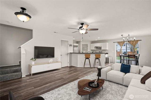 living area featuring ceiling fan with notable chandelier, stairway, and dark wood-style floors