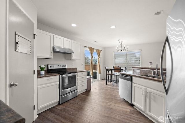 kitchen featuring dark wood-style flooring, a sink, under cabinet range hood, appliances with stainless steel finishes, and dark countertops