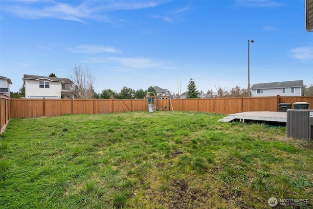 view of yard featuring a wooden deck, a fenced backyard, and a playground