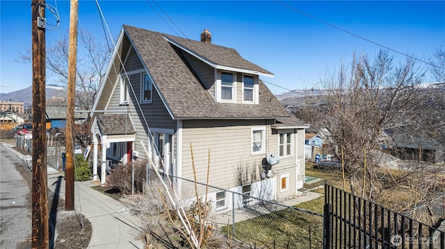 view of side of home featuring a shingled roof, fence, and a mountain view