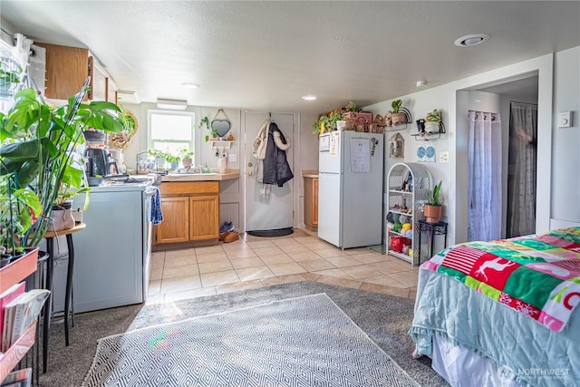 kitchen with brown cabinets, light tile patterned floors, light countertops, freestanding refrigerator, and a sink