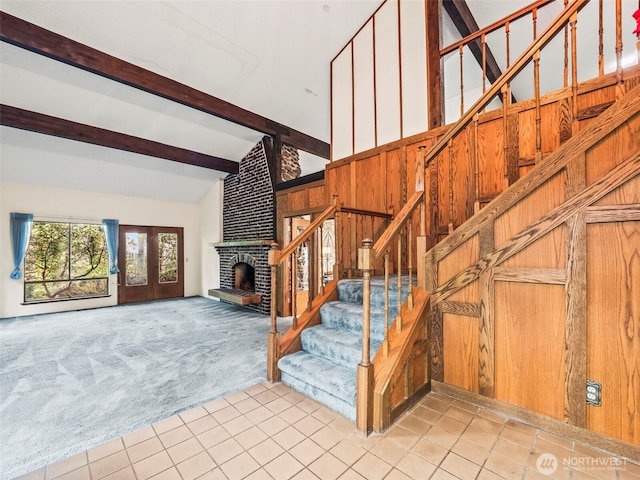 staircase featuring wooden walls, carpet flooring, a brick fireplace, beam ceiling, and tile patterned floors