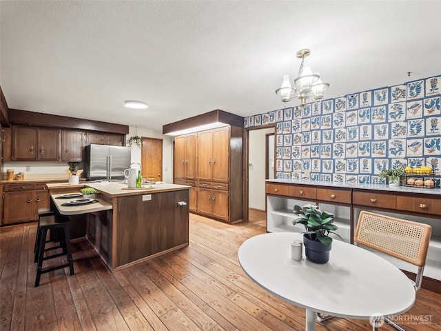 kitchen featuring a center island with sink, hardwood / wood-style flooring, high quality fridge, light countertops, and a chandelier