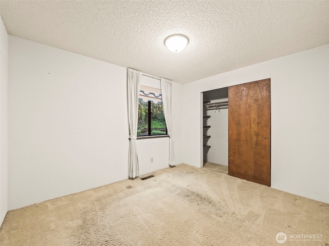 unfurnished bedroom featuring a textured ceiling, carpet floors, a closet, and visible vents