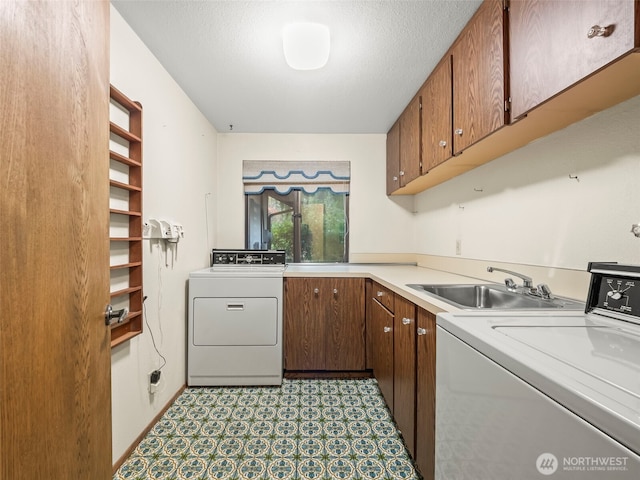 laundry area featuring a textured ceiling, washing machine and dryer, a sink, cabinet space, and light floors