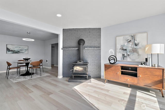 living room featuring light wood-type flooring, a wood stove, and baseboards