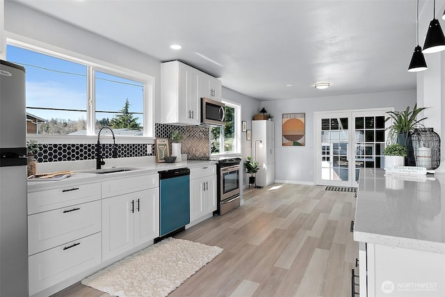 kitchen featuring tasteful backsplash, light wood-style flooring, appliances with stainless steel finishes, white cabinetry, and a sink