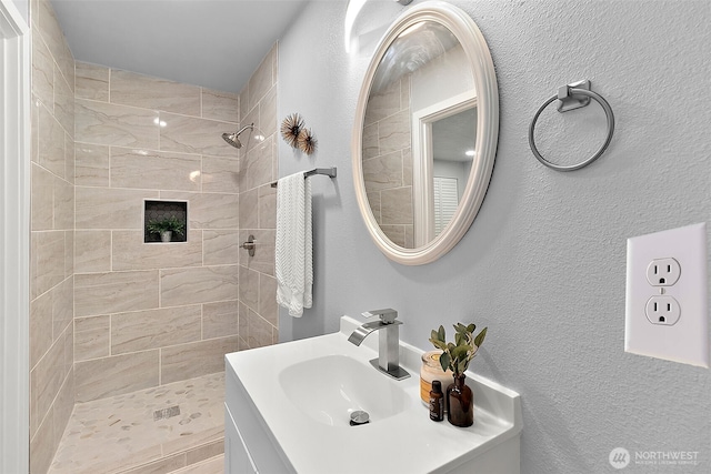 full bath featuring a textured wall, a tile shower, and vanity