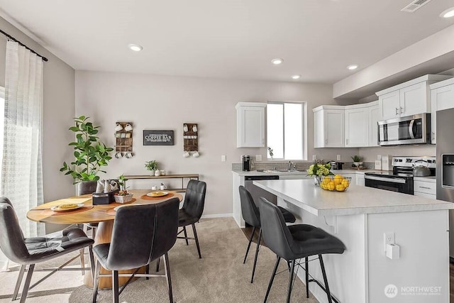 kitchen featuring a breakfast bar, stainless steel appliances, light countertops, white cabinetry, and a sink