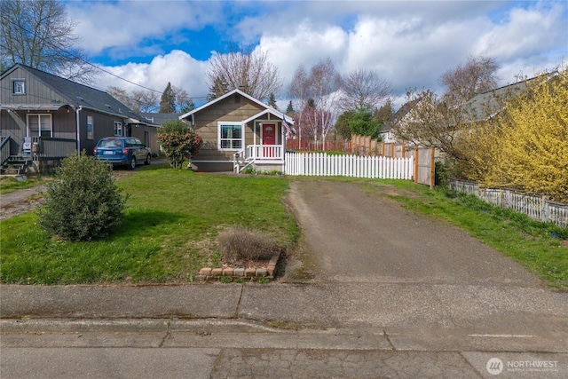 bungalow featuring dirt driveway, fence, and a front lawn