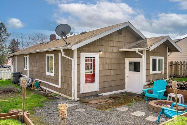 rear view of house with an outdoor fire pit, a chimney, fence, and a shingled roof