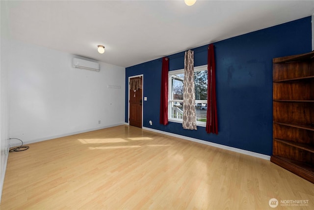 unfurnished room featuring an AC wall unit, wood finished floors, and baseboards