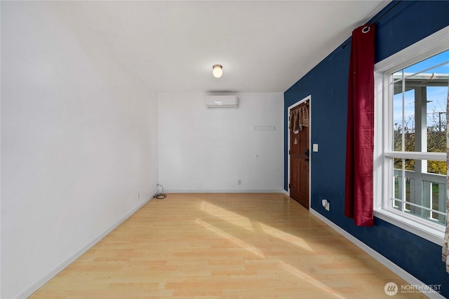 empty room featuring a wall unit AC, baseboards, and wood finished floors