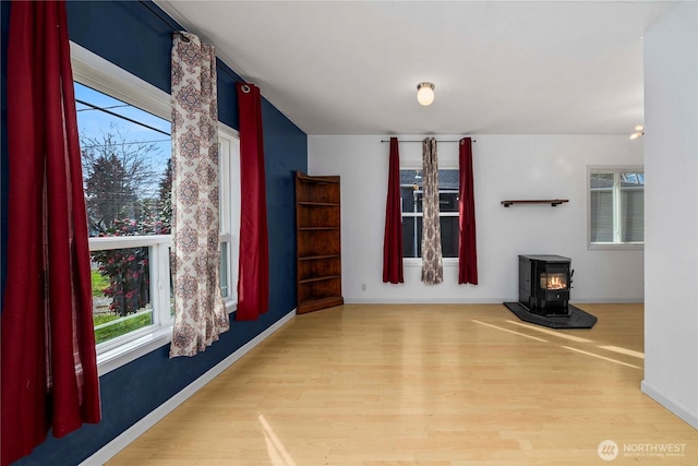 unfurnished living room featuring a wood stove, a wealth of natural light, baseboards, and wood finished floors