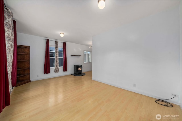 unfurnished living room with a wood stove, baseboards, and wood finished floors