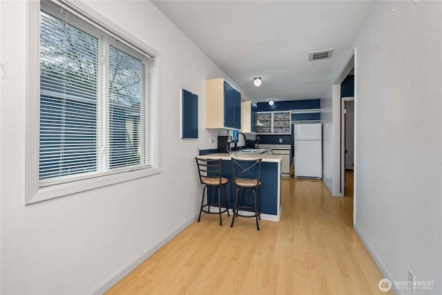 kitchen featuring a peninsula, a sink, visible vents, light wood-style floors, and freestanding refrigerator