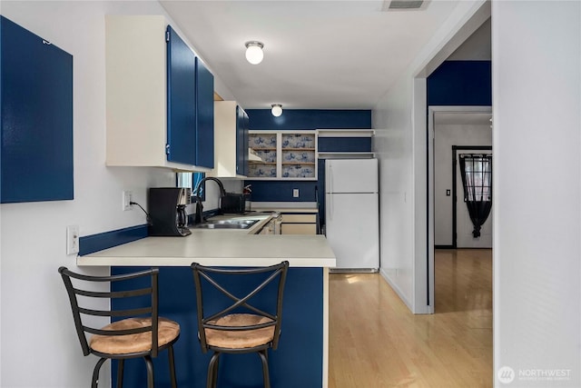 kitchen featuring a sink, light wood-style floors, light countertops, blue cabinetry, and freestanding refrigerator