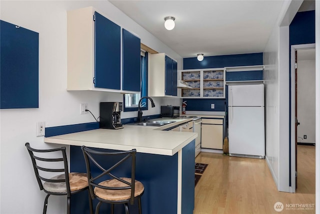 kitchen with a peninsula, white appliances, a sink, light countertops, and blue cabinetry