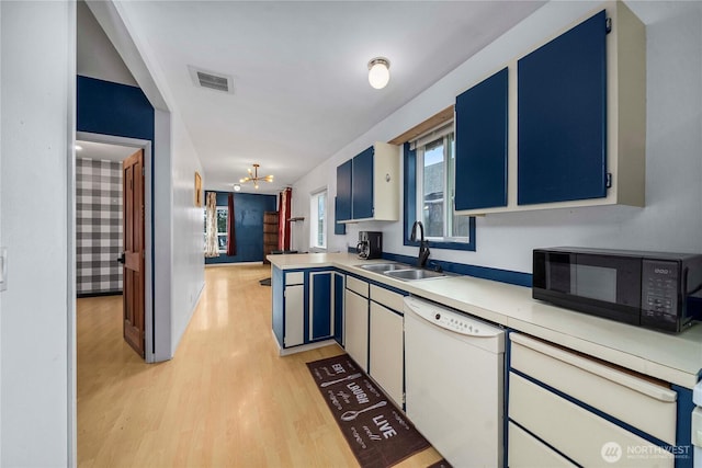 kitchen featuring black microwave, white dishwasher, a sink, visible vents, and light countertops