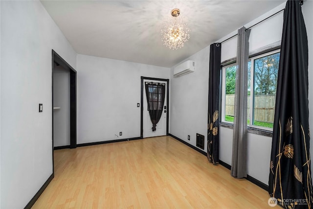 spare room with visible vents, baseboards, light wood-style flooring, a wall mounted air conditioner, and a chandelier