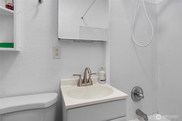 full bathroom with a textured wall, shower / bath combination, vanity, and toilet