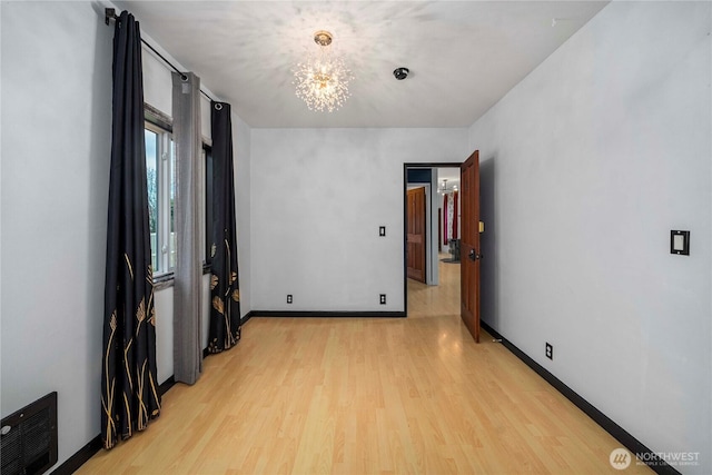 empty room with a chandelier, light wood-type flooring, visible vents, and baseboards