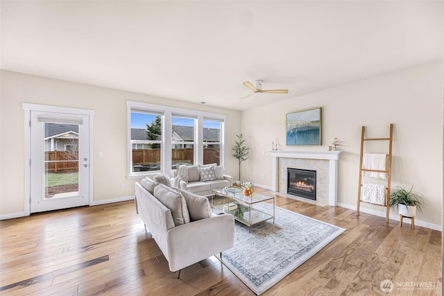 living area featuring light wood-style floors, a fireplace, baseboards, and a ceiling fan