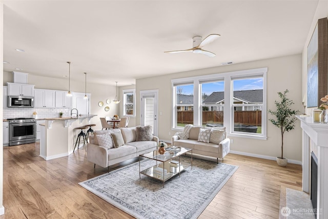 living area with light wood-style flooring, baseboards, ceiling fan, and a fireplace with flush hearth