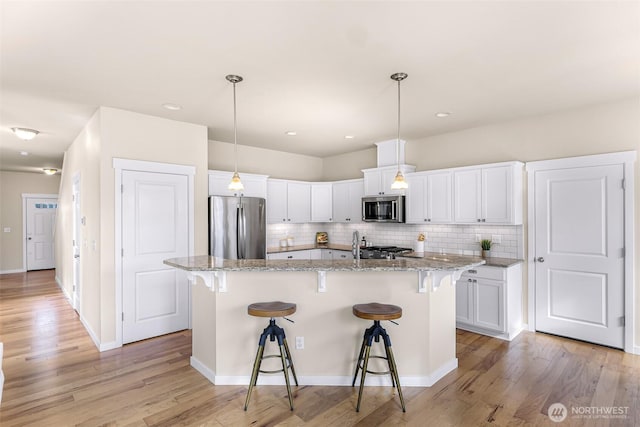 kitchen with stainless steel appliances, light wood-style flooring, a kitchen bar, and white cabinetry