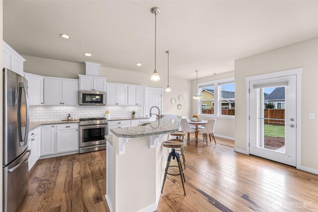 kitchen with appliances with stainless steel finishes, backsplash, hardwood / wood-style floors, and white cabinetry