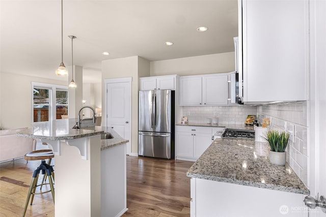 kitchen featuring wood finished floors, backsplash, freestanding refrigerator, a sink, and light stone countertops