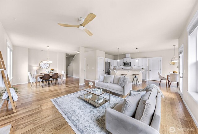 living area with ceiling fan with notable chandelier, light wood-type flooring, and baseboards