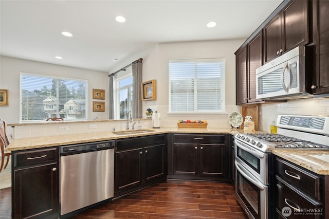 kitchen featuring dark wood-type flooring, a peninsula, light stone countertops, stainless steel appliances, and a sink