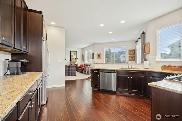 kitchen with light stone counters, a sink, stainless steel dishwasher, and dark wood-style floors