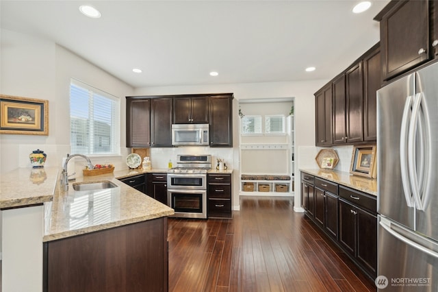 kitchen with dark brown cabinetry, decorative backsplash, appliances with stainless steel finishes, light stone counters, and a sink