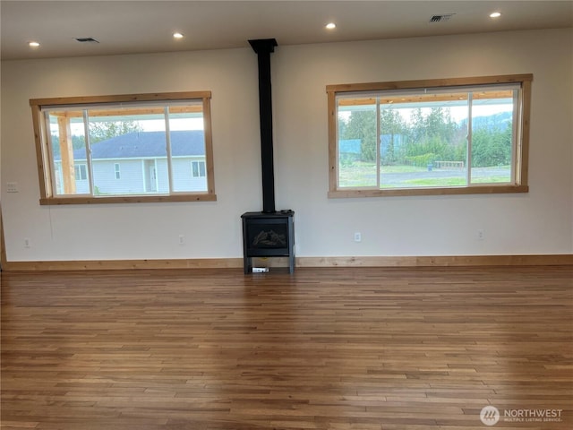 unfurnished living room featuring a wood stove, a healthy amount of sunlight, visible vents, and wood finished floors