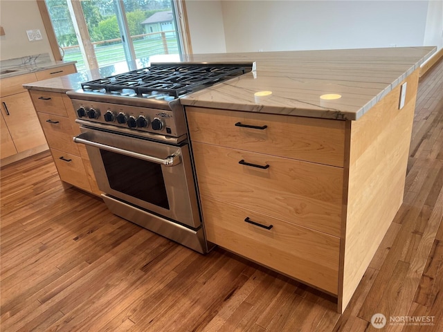 kitchen featuring light brown cabinetry, light stone counters, high end stove, and light wood-style flooring