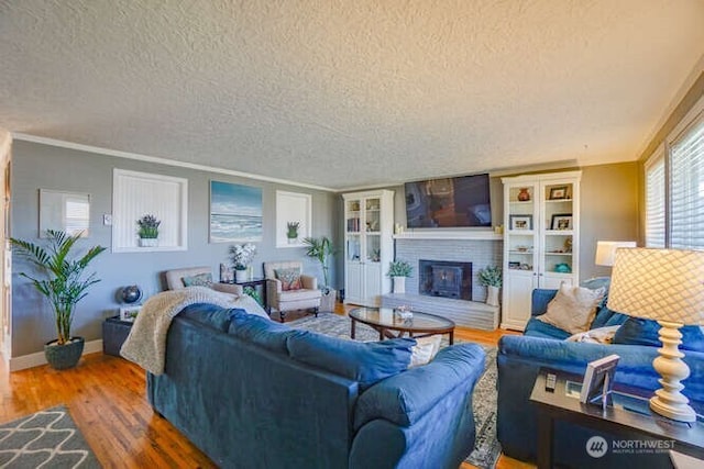 living room with a brick fireplace, crown molding, a textured ceiling, and wood finished floors