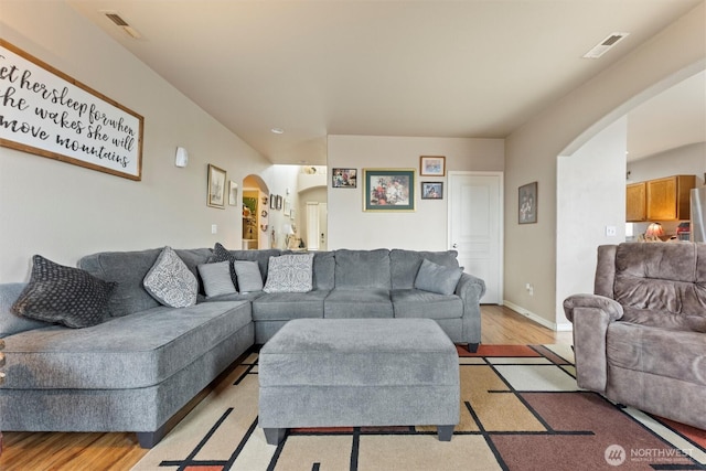 living area with visible vents, arched walkways, and light wood-style flooring